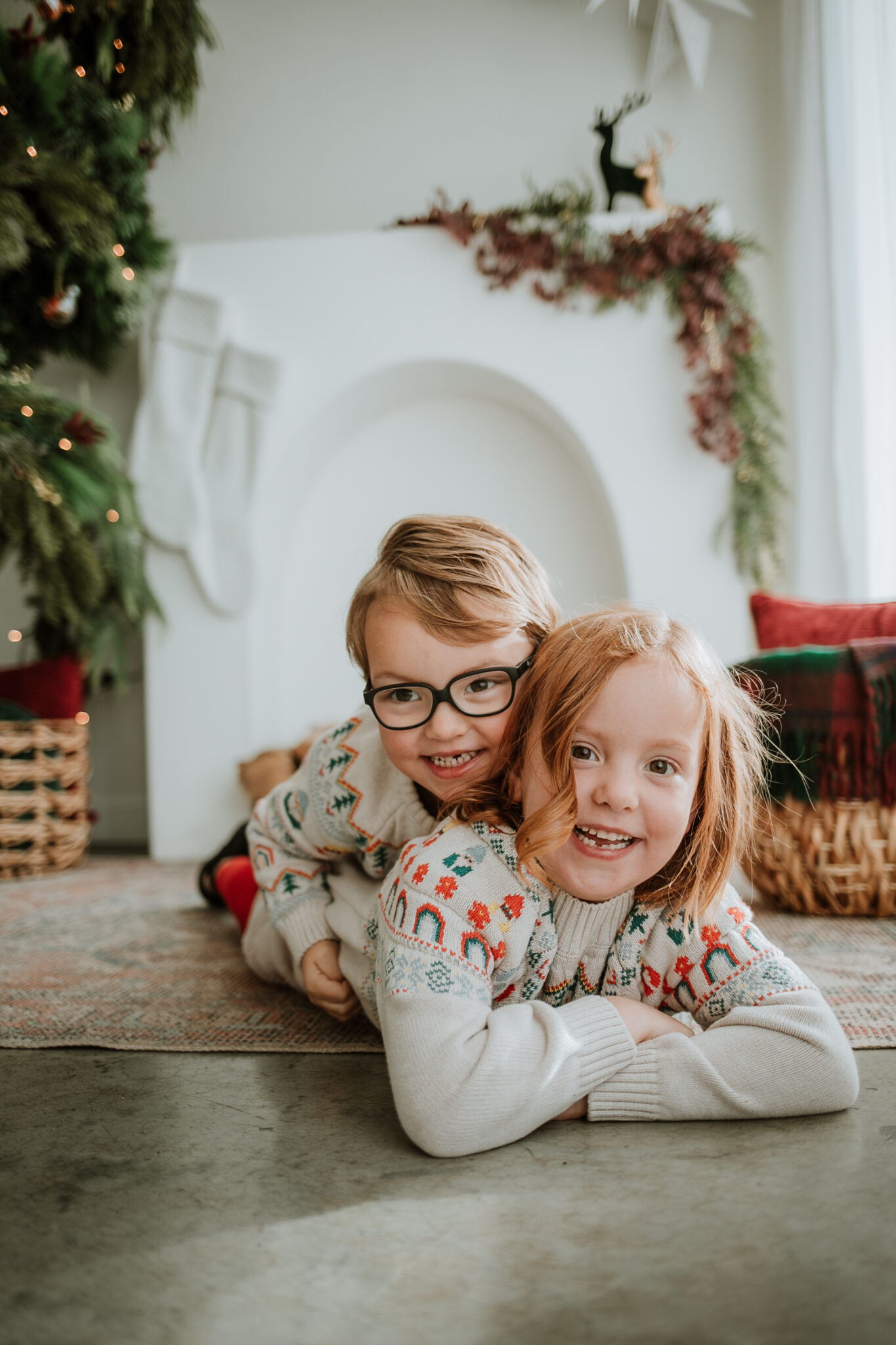 Two children in matching holiday pajamas giggling in front of a Christmas tree and glowing fairy lights during a holiday mini session in Longmont, CO.