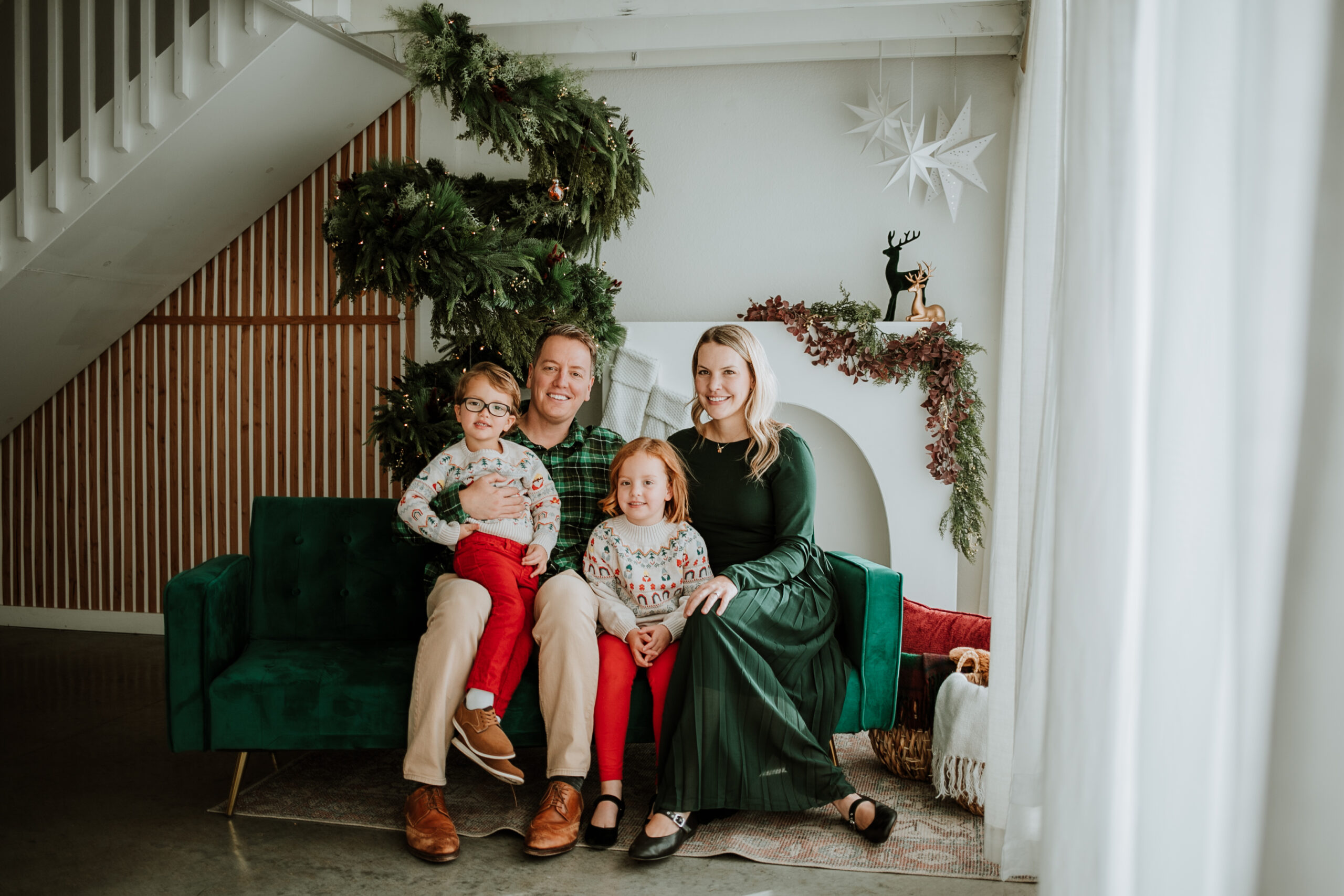 Smiling family of three standing together in a festive holiday studio with twinkling lights and Christmas décor in Longmont, Colorado.