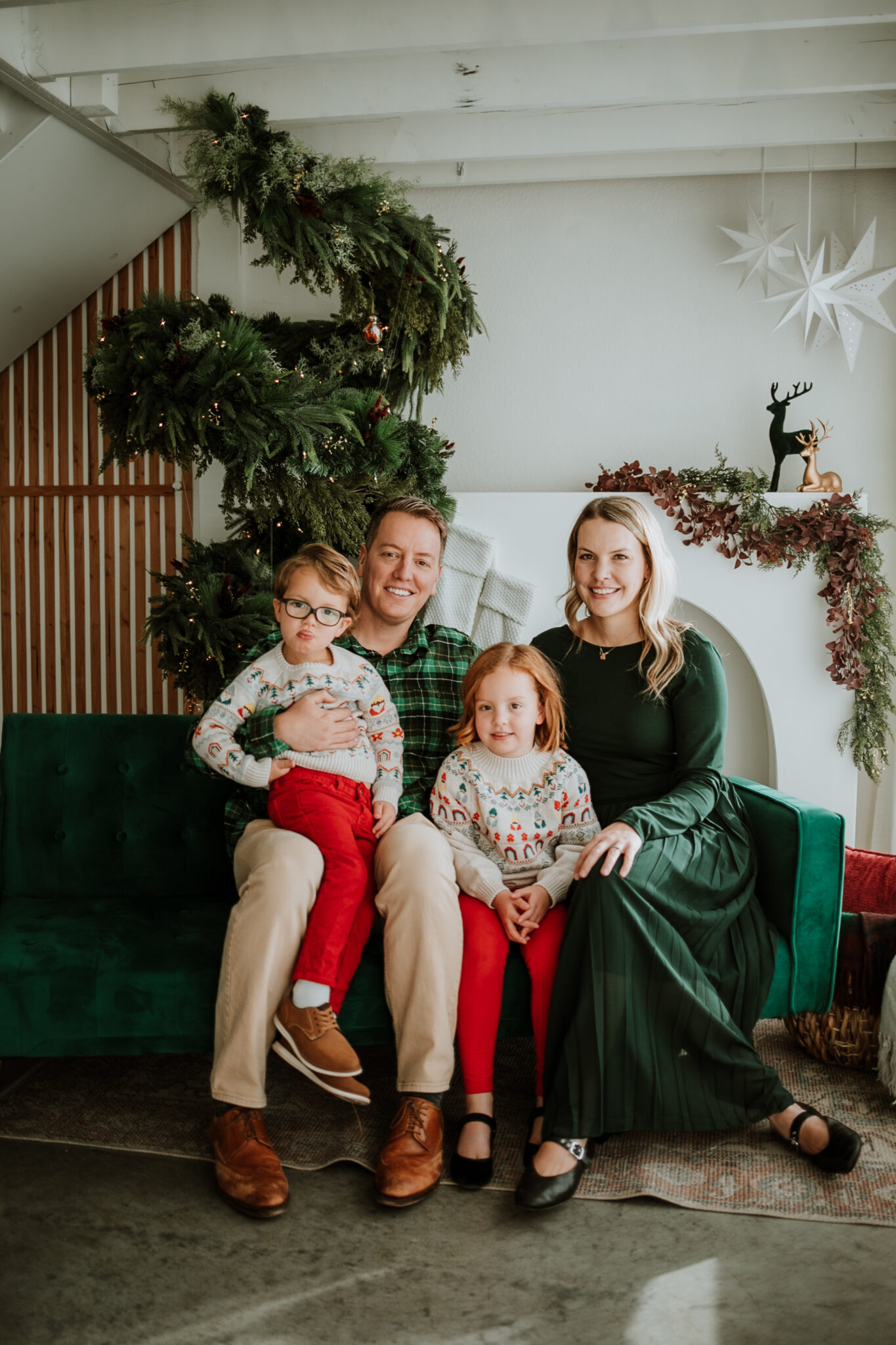 Family of four smiling and snuggled together on a cozy holiday studio set with twinkling lights and festive décor in Longmont, Colorado.