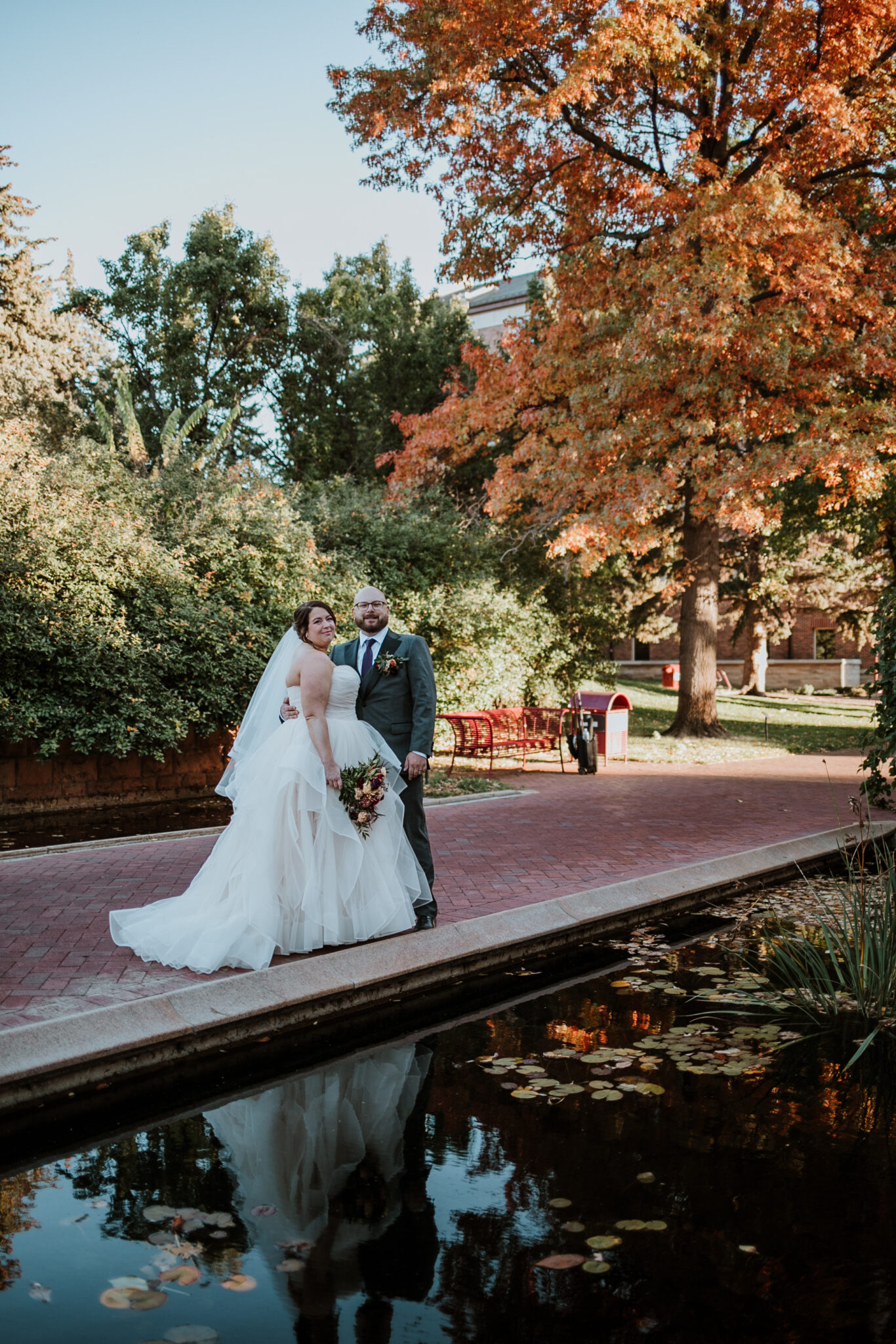 newlyweds walking through tree lined path at University of Denver in autumn